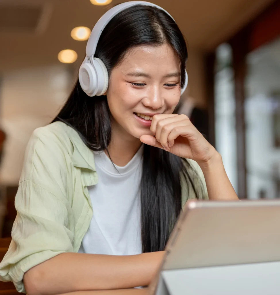 woman wearing headphones, smiling at her laptop